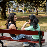 Two teenage girls talking on a park bench outdoors.