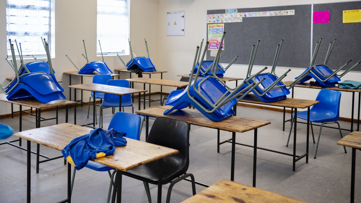 An empty classroom with most chairs on top of the desk except for two.