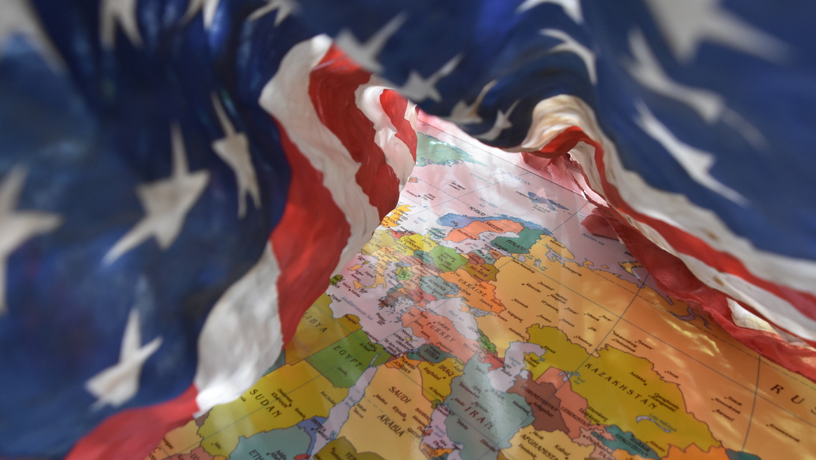 A flag of the United States waves over a map of the world.