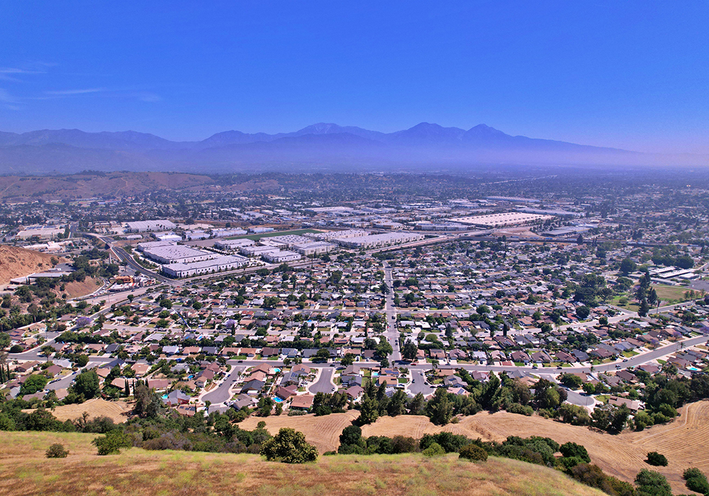 Dozens of single-family homes on small lots along low-traffic residential streets in front of large-footprint industrial uses, with the San Gabriel Mountains in the background.