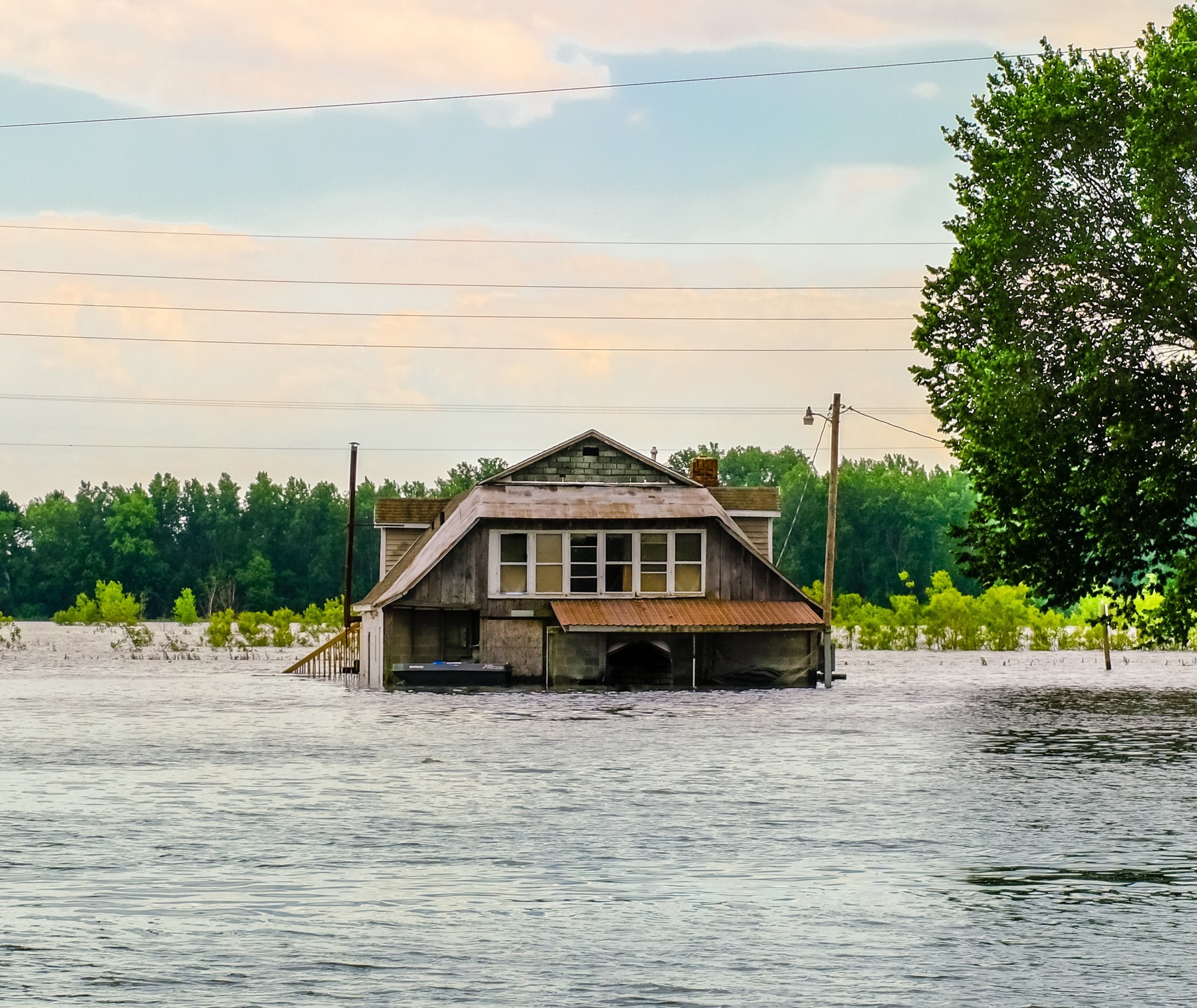 A weathered two-story wooden house sits abandoned in the midst of flooded fields.