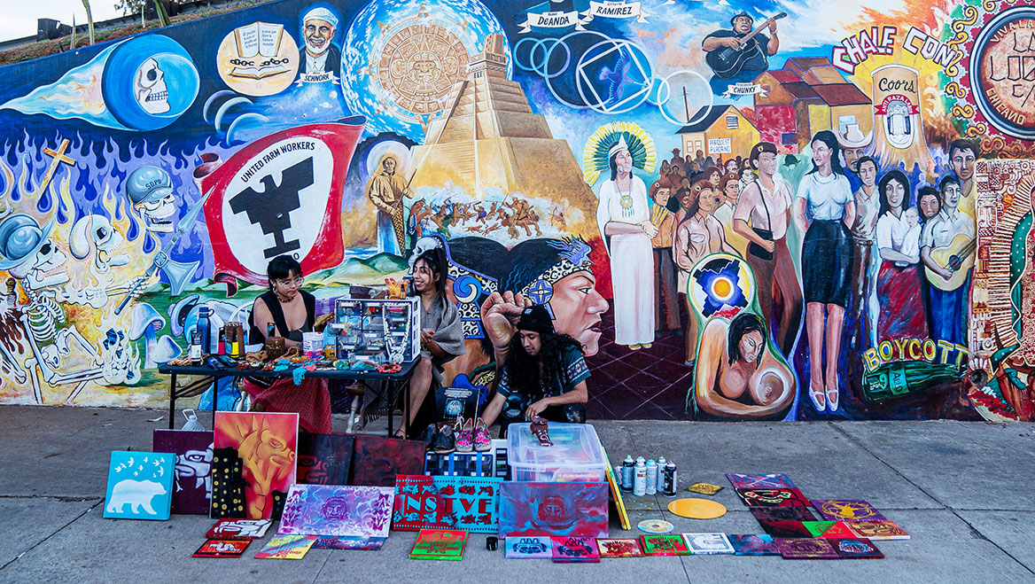 A vendor sells handcrafted native art in front of one of Chicano Park’s murals that reflects the neighborhood’s Indigenous and Hispanic culture and history.