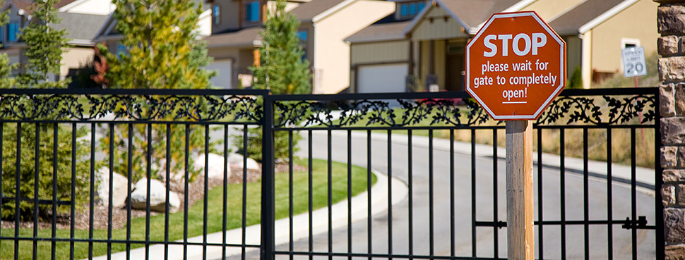 A gated residential community with a sign in front of the access gate reading, "STOP please wait for gate to completely open!"