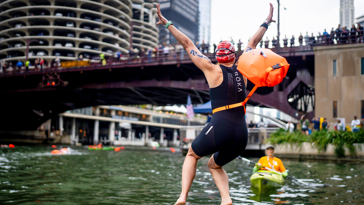 A person is in midair after jumping into a river in a city.