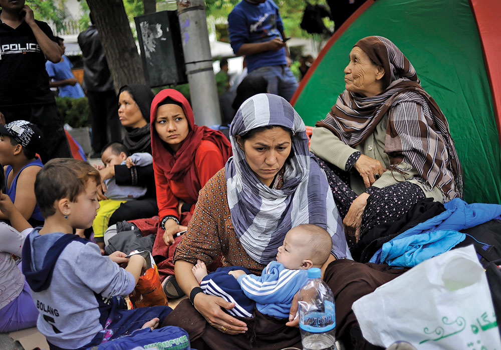 Migrants sit outside their tents in Victoria Square in 2015. Many stay in Athens temporarily before trying to continue their trip to more prosperous northern European countries. Photo by AP Photo/Fotis Plegas G.