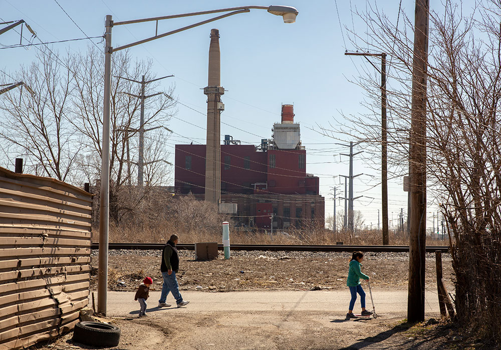 A family walks next to a railroad track near the Crawford Generating Station in Little Village in Chicago. A contributor to neighborhood respiratory illnesses until it was forced to close in 2012, the 95-year-old building is now being demolished and the site remediated to make way for a million-square-foot distribution center — something residents fear will be another harmful polluter.