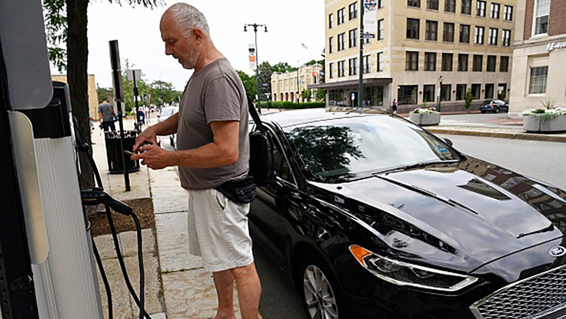 Laurence Kelly finishes a transaction at the EV charging station in front of Portland, Maine's city hall. By charging a fee for electricity, the city will now break even on its charging stations. Photo by Shawn Patrick Ouellette/Portland Press Herald/Getty Images.