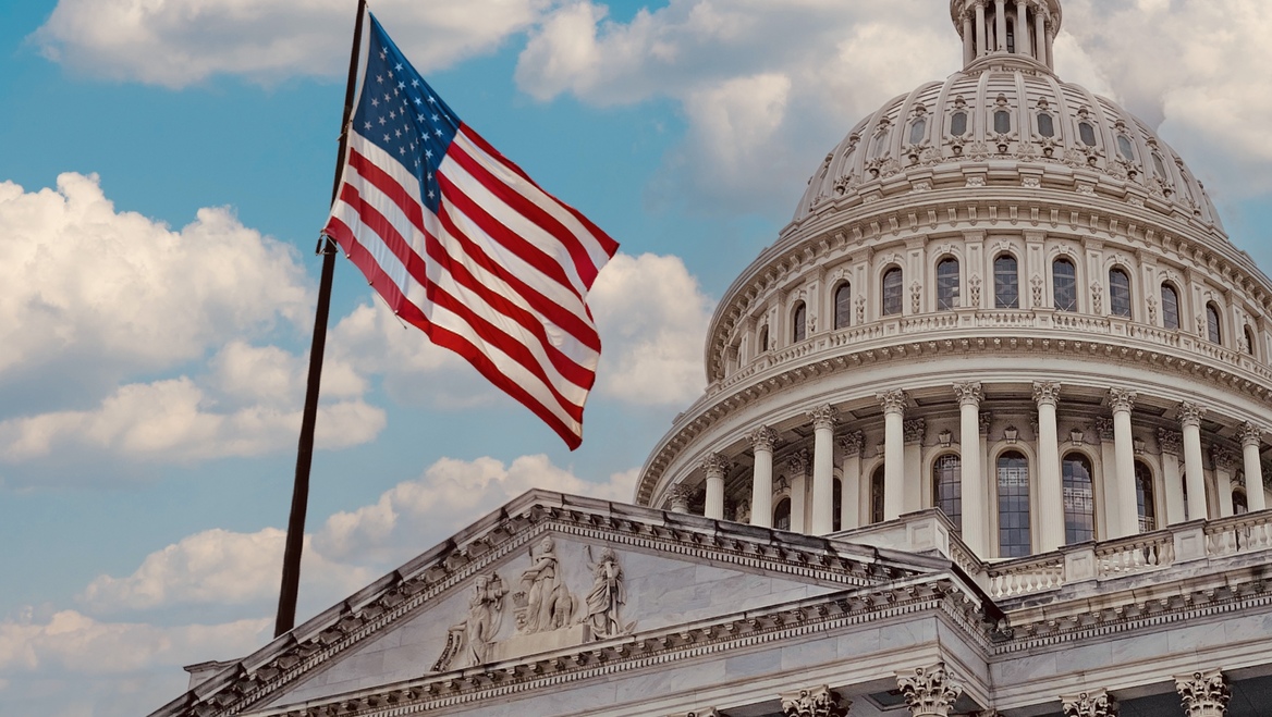 The US Capitol building with the American flag waving in the foreground.