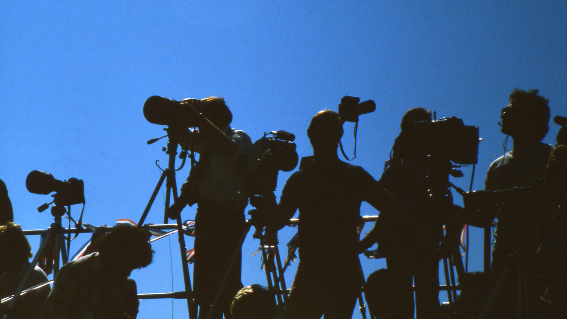 People in shadow with cameras and a blue background.