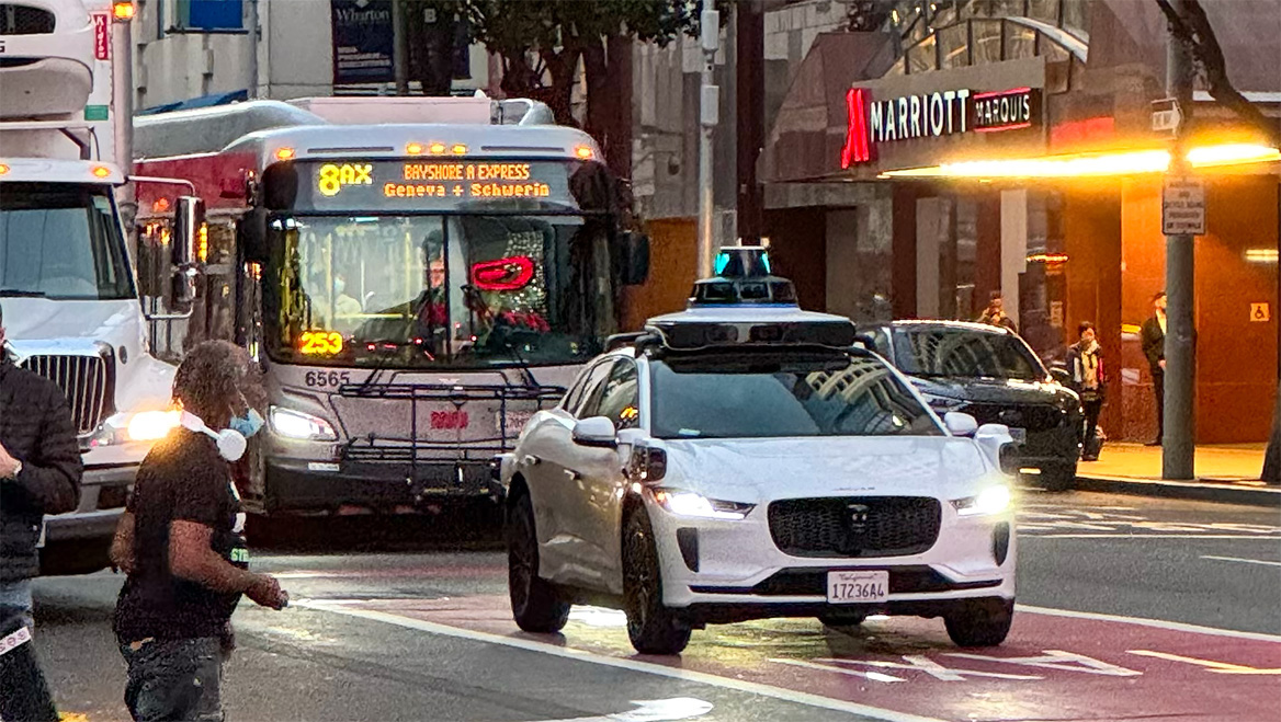 A Waymo AV taxi and city bus compete for space in San Francisco, California. Photo by Chris Arvin.