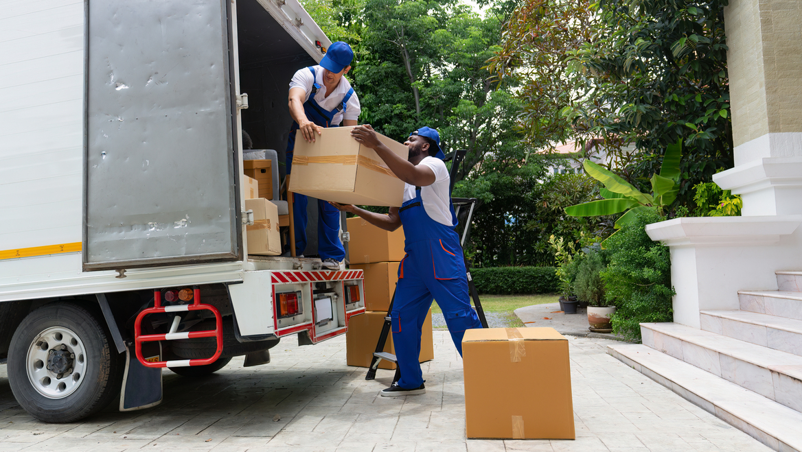 Two movers put cardboard boxes into a truck.