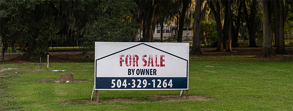 A sign that says For Sale By Owner in a grassy field, with trees in the background