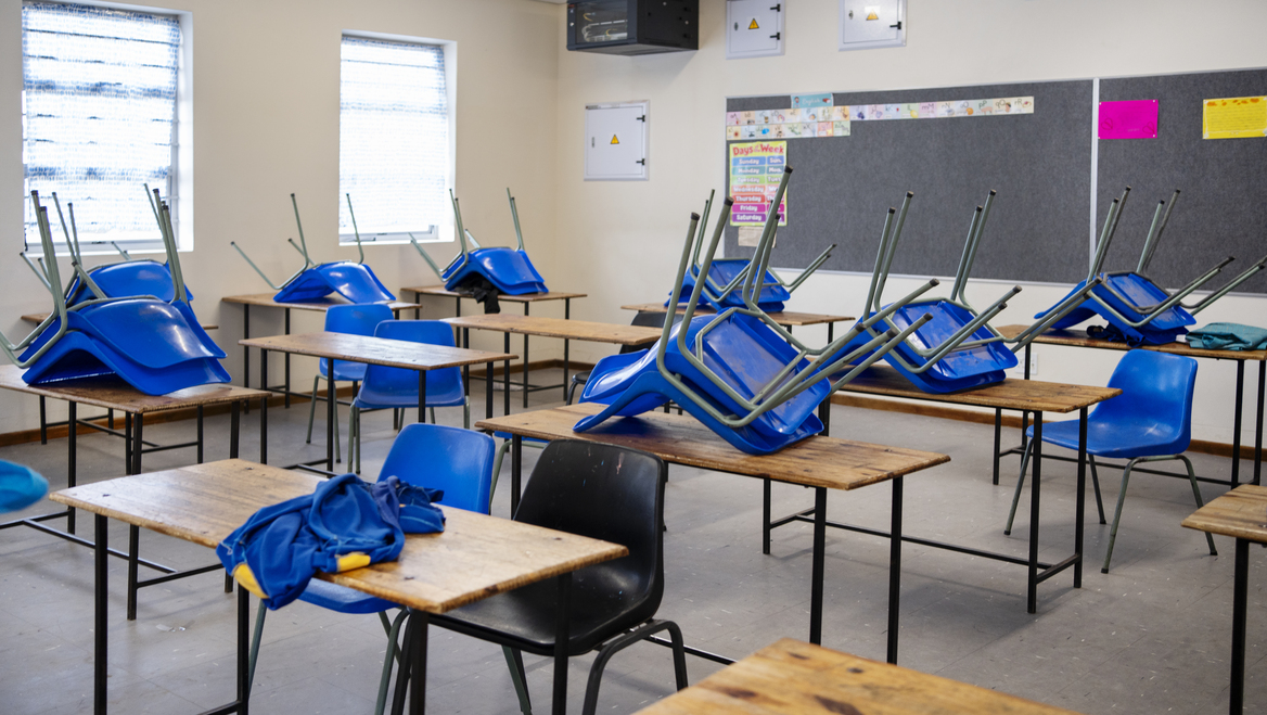 An empty classroom with most chairs on top of the desk except for two.