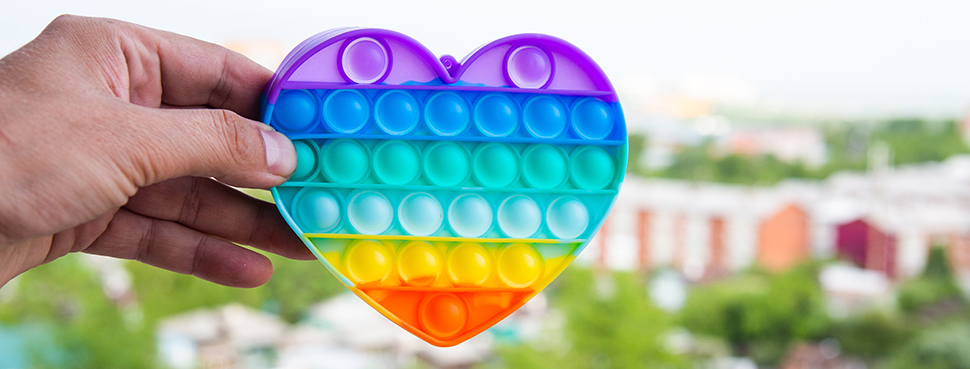 A hand holding a heart-shaped pop-it up, with a medium-density urban environment in the background.