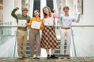 Four students stand celebrating with certificates