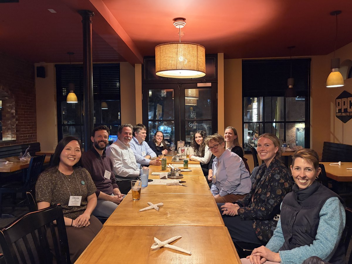 A group of about twelve adults sit around a long wooden table.
