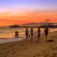 People walking on the beach at sunset near a pier and Ferris wheel