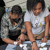 Three women collaborate on a community map, adding heart-shaped notes with handwritten text.