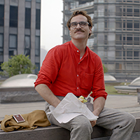 Joaquin Phoenix in "Her" sits outdoors with lunch, wearing a red shirt and mustache