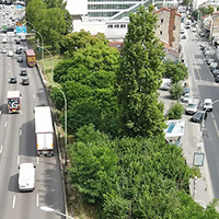 Busy urban highway with heavy traffic, separated by lush green trees and adjacent city street.