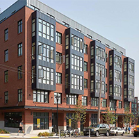 Modern brick apartment building in a city neighborhood with people crossing the street.