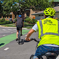 Three cyclists wearing helmets on a green bike lane in a leafy suburban area