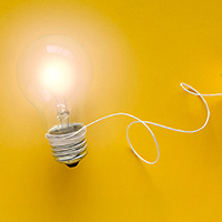 Bright lightbulb connected by string to a yellow paper airplane on a yellow background.
