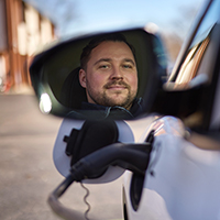 Man reflected in side mirror of electric car charging