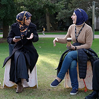 Group of diverse students in hijabs chatting outdoors with coffee cups on campus.