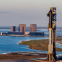 SpaceX Starship rocket on launchpad at Boca Chica, with SpaceX facilities in background.