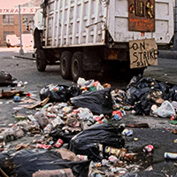 Garbage truck and strike sign amid overflowing trash during a sanitation strike.