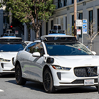 Row of white Jaguar I-PACE electric cars at a city intersection.