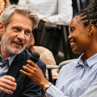 Man and woman in audience at a conference, discussing with microphone.