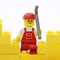 Lego construction worker standing in a hole in a yellow brick wall.