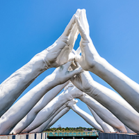 Sculpture of giant white hands forming an archway over water in Venice.