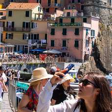 Tourists in colorful Cinque Terre village, Italy, with buildings on a cliffside.