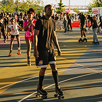 Diverse group of people rollerblading on an outdoor court with colorful markings.