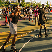 Diverse group of people rollerblading on an outdoor court with colorful markings.