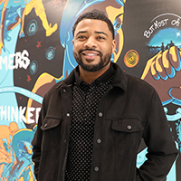 Man in front of mural with text "The Dreamers, the Thinkers" and "But Most of All.