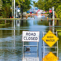 Flooded street with "Road Closed" and "High Water" signs, indicating a natural disaster.