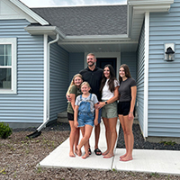 Family poses for a photo in front of their new light blue home.