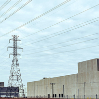 Tall power line towers and industrial buildings under a cloudy sky.