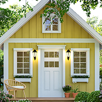 Charming yellow tiny house with white trim and flower boxes in a lush garden.