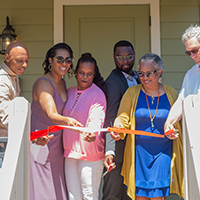 Group cutting ribbon at new home, celebrating affordable housing.