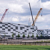 Construction cranes poised over massive, single-story, windowless industrial structures.