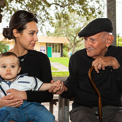 A young mother and her baby sit on a porch with an older male, who may be a grandfather.