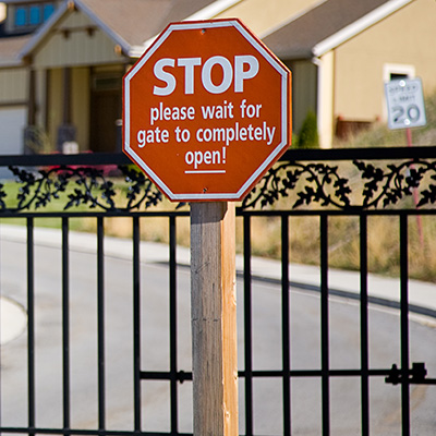 A gated residential community with a sign in front of the access gate reading, "STOP please wait for gate to completely open!"