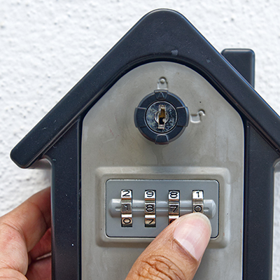 A hand sets the code on a residential key box shaped like a home.