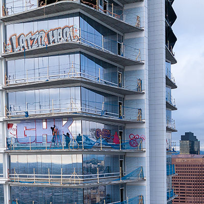 Graffiti artists spray painting the unfinished upper floors of a high-rise structure.