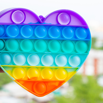 A hand holding a heart-shaped pop-it up, with a medium-density urban environment in the background.